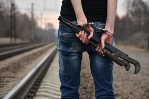 The girl in handcuffs with the pipe wrench on the railway track background. The concept of crime prevention with the participation of the railway and trains. photo