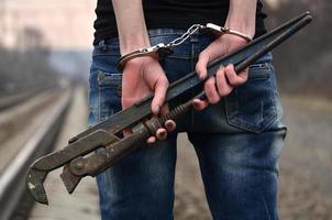 The girl in handcuffs with the pipe wrench on the railway track background. The concept of crime prevention with the participation of the railway and trains. photo