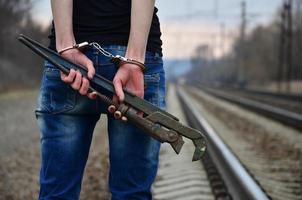 The girl in handcuffs with the pipe wrench on the railway track photo