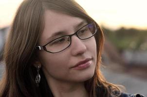 Girl in glasses and jeans jacket is resting on the roof of a hou photo