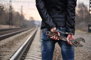 la chica esposada con la llave ajustable en el fondo de la vía férrea. el concepto de prevención del delito con la participación del ferrocarril y los trenes. foto