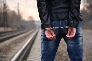 Girl in handcuffs on the background of a railway track. The concept of crime prevention with the participation of the railway and trains. Evening photo of the lower half of the body of a girl