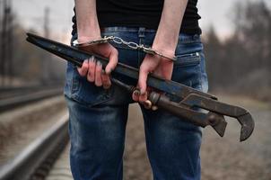 la chica esposada con la llave de tubo en el fondo de la vía férrea. el concepto de prevención del delito con la participación del ferrocarril y los trenes. foto