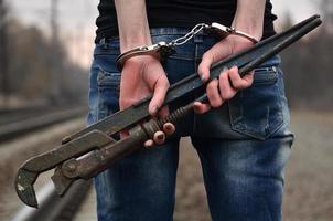 la chica esposada con la llave de tubo en el fondo de la vía férrea. el concepto de prevención del delito con la participación del ferrocarril y los trenes. foto