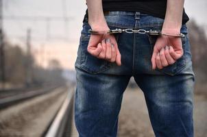 Girl in handcuffs on the background of a railway track. The concept of crime prevention with the participation of the railway and trains. Evening photo of the lower half of the body of a girl