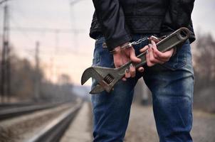 The girl in handcuffs with the adjustable wrench on the railway track background. The concept of crime prevention with the participation of the railway and trains. photo