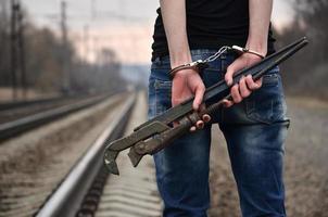 la chica esposada con la llave de tubo en el fondo de la vía férrea. el concepto de prevención del delito con la participación del ferrocarril y los trenes. foto