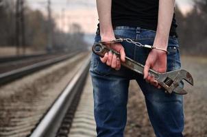 la chica esposada con la llave ajustable en el fondo de la vía férrea. el concepto de prevención del delito con la participación del ferrocarril y los trenes. foto