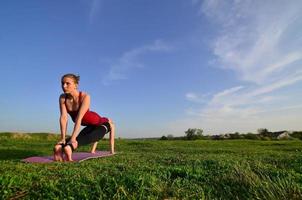 dos jóvenes de pelo limpio con trajes deportivos practican yoga en una pintoresca colina verde al aire libre por la noche. el concepto de deporte haciendo ejercicio al aire libre foto