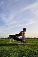 dos jóvenes de pelo limpio con trajes deportivos practican yoga en una pintoresca colina verde al aire libre por la noche. el concepto de deporte haciendo ejercicio al aire libre foto