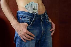 The body of a guy in blue jeans with a lot of dollar bills, visible from under the clothes photo