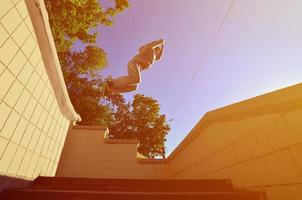 A young guy performs a jump through the space between the concrete parapets. The athlete practices parkour, training in street conditions. Bottom view photo