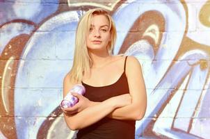 A young and beautiful sexy girl graffiti artist with a paint spray stands on the wall background with a graffiti pattern in blue and purple tones photo