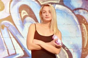 una joven y hermosa artista de graffiti sexy con un spray de pintura se encuentra en el fondo de la pared con un patrón de graffiti en tonos azules y morados foto