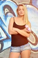 A young and beautiful sexy girl graffiti artist with a paint spray stands on the wall background with a graffiti pattern in blue and purple tones photo