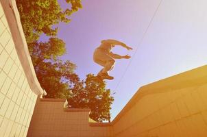 A young guy performs a jump through the space between the concrete parapets. The athlete practices parkour, training in street conditions. Bottom view photo