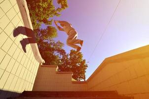 A young guy performs a jump through the space between the concrete parapets. The athlete practices parkour, training in street conditions. Bottom view photo