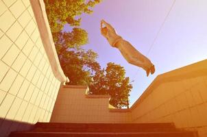 A young guy performs a jump through the space between the concrete parapets. The athlete practices parkour, training in street conditions. Bottom view photo