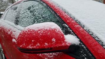 Snow is falling on a red car in the street close-up. Winter is hungry. video