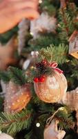 video vertical, chica irreconocible decora un árbol de navidad con bolas festivas. luces cálidas de guirnaldas parpadean en el fondo. vacaciones año nuevo. ambiente invernal, concepto de tradición.