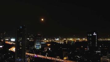 metraje de timelapse, noche de luna llena por el río chaophraya con atasco de tráfico en la carretera en primer plano, bangkok, tailandia video