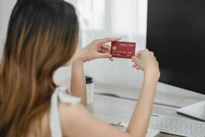 Woman holding showing credit card to shopping online. asian woman working at home. Online shopping, e-commerce, internet banking, spending money, working from home concept. photo