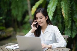 Freelance business woman calling on mobile smartphone while working with laptop, businesswoman mobile phone to calling with customers or shopping online. Smart phone conversation conferrence. photo