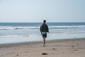 Rear view of man with towel walking at beach in summer photo