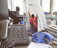 landline phone in the office on the table. black handset with buttons and display. means of communication in the office. stationery next to the phone photo