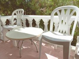 muebles de plástico en el balcón. pequeña mesa redonda con sillas blancas. lugares para el descanso de turistas y personas. balcón a una altura contra el telón de fondo de un bosque de abetos foto