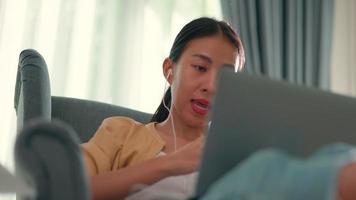 handhållen, stänga upp skott ung kvinna använda sig av hörlur och bärbar dator dator till video konferens uppkopplad medan arbete från Hem