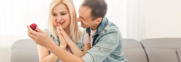 Man surprising his girlfriend with a gift on the couch at home in the living room photo