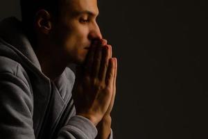 Religious young man praying to God on dark background, black and white effect photo