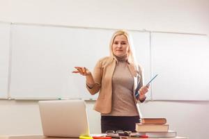 retrato de una linda maestra sosteniendo blocs de notas en un salón de clases en la escuela foto