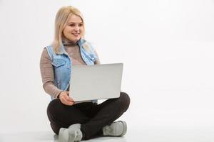 mujer joven con laptop sentada en el piso cerca de la pared clara foto
