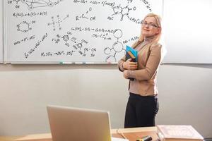 profesor enseñando a contar con pizarra en el aula. mujer rubia sonriente explicando las adiciones en la columna en clase. profesor de matemáticas explicando sumas aritméticas a niños de primaria. foto