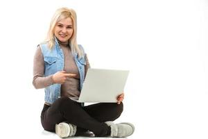 retrato de una chica casual sonriente sosteniendo una computadora portátil mientras se sienta en un piso aislado sobre fondo blanco foto
