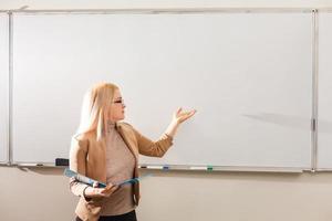 retrato de una linda maestra sosteniendo blocs de notas en un salón de clases en la escuela foto