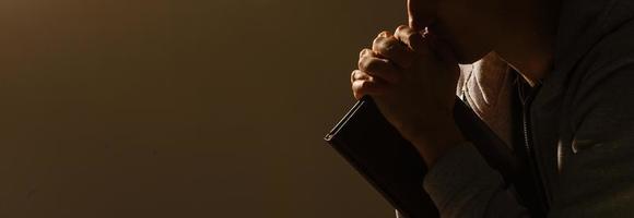 Religious young man praying to God on dark background, black and white effect photo