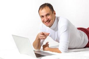 Happy young man lies on a floor and using laptop isolated over white background photo