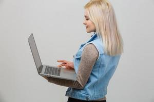 Happy young woman using laptop on gray background photo