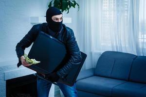 Robber man dressed in black hoodie stands with disguised face and holds a lot of money in his hands, stole a large amount, a thief man stole a TV photo