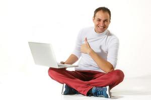 Happy young man sitting on a floor and using laptop isolated over white background photo