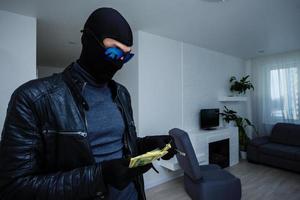 Robber man dressed in black hoodie stands with disguised face and holds a lot of money in his hands, stole a large amount, a thief man stole a TV photo