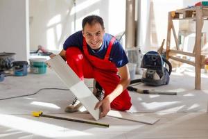 el maestro lleva ropa de trabajo, está comprobando el horizonte de la instalación de azulejos, usando el nivel de construcción, ajustando, trabajos de reparación profesional foto