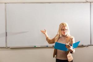 Portrait of pretty teacher holding notepads in a classroom in school photo