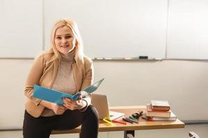 retrato de una linda maestra sosteniendo blocs de notas en un salón de clases en la escuela foto