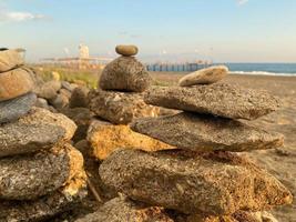 A pyramid of stones stacked on top of each other on the beach and sand with small natural multi-colored stones on the shore against the backdrop of the sea at sunset photo