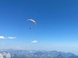 el hombre en parapente está volando en el aire usando un paracaídas sobre las montañas detrás del cielo azul. deportes extremos y libertad foto