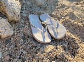 White flip flops on sand near sea, space for text. Beach accessories photo